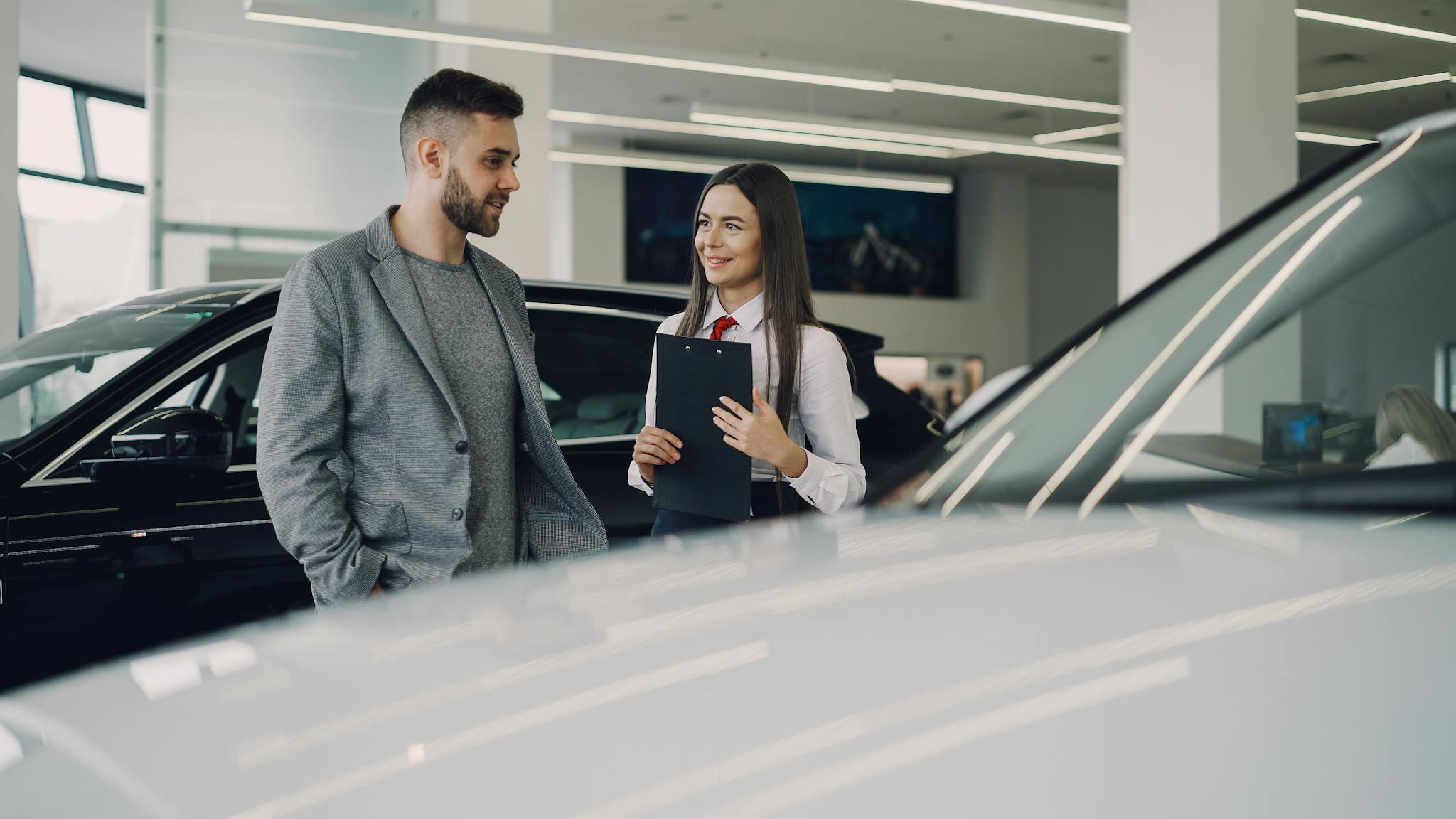 Man consults with salesperson in modern car dealership showroom.