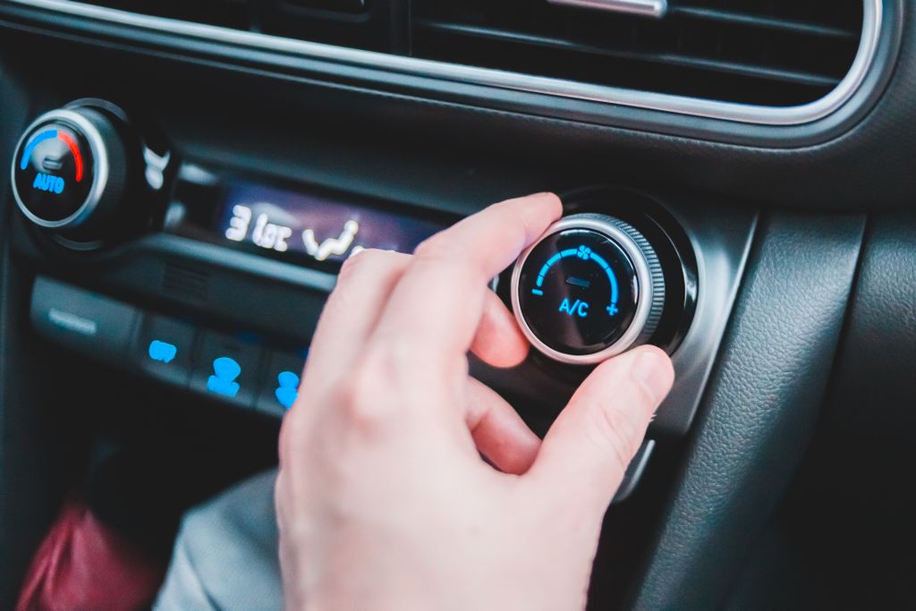Crop anonymous person regulating temperature in car using controller on panel while sitting in car